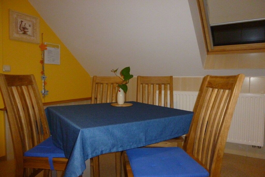A dining area with a table covered by a blue tablecloth, wooden chairs, and a potted plant on the table.