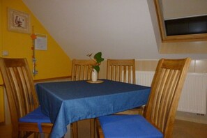 A dining area with a table covered by a blue tablecloth, wooden chairs, and a potted plant on the table. - Holiday apartment with 1 bedroom (Märkische Heide)