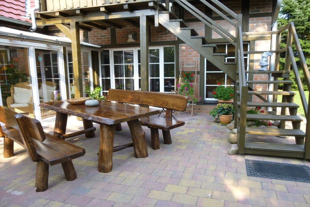 An outdoor patio with a wooden table and benches, a brick wall, and a staircase leading to an upper level.