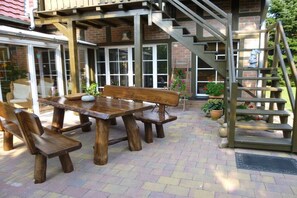 Eine Außenpatio mit Holztisch und -bänken, einer Backsteinmauer und einer Treppe, die zu einer erhöhten Ebene führt.