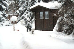 A wooden cabin with a snow-covered roof, surrounded by snow-laden trees. - Holiday apartment with 1 bedroom (Märkische Heide)