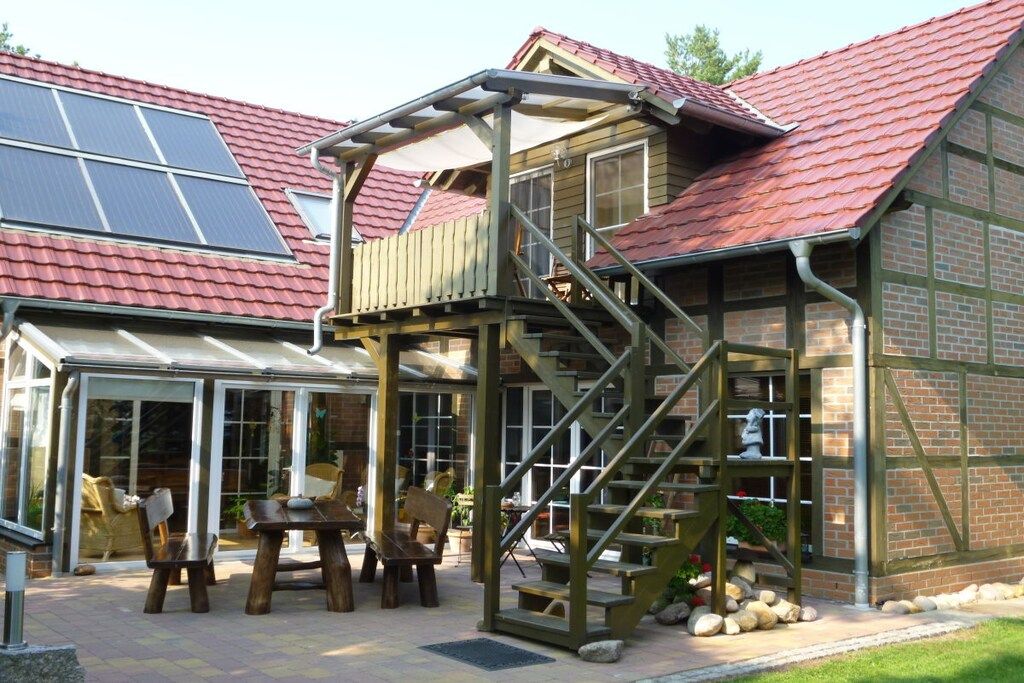 Una terraza de madera con una escalera, un patio cubierto y un edificio de ladrillo con techo rojo.