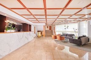 Un hall d’entrée moderne avec un comptoir de réception en marbre, un escalier et des sièges contemporains.