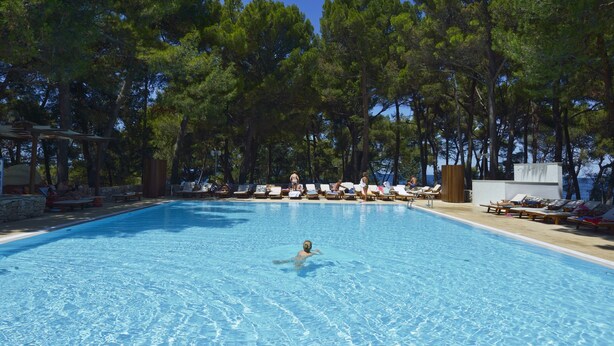 Una piscina rodeada de sillas de descanso y árboles.