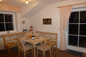 A dining area with a wooden table and chairs, a bottle of wine, and a fruit bowl. - Country House Glockner Dream (Heiligenblut am Großglockner)
