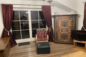 A living room with a sofa, ottoman, television, and a cabinet with intricate designs. - Country House Glockner Dream (Heiligenblut am Großglockner)