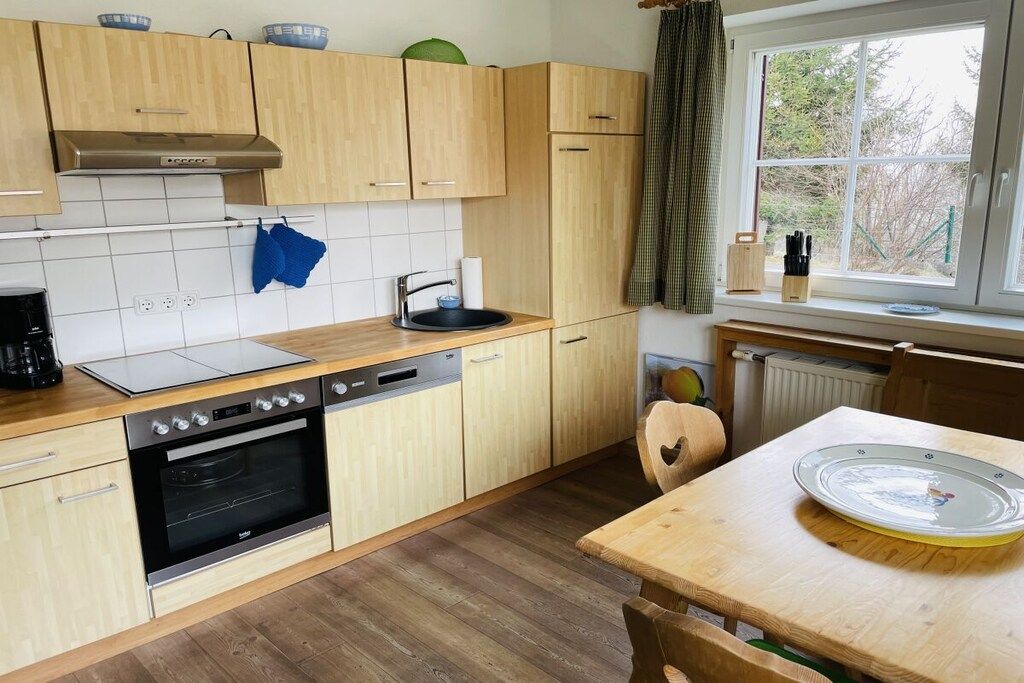 A compact kitchen with wooden cabinets, a built-in oven, a sink, and a window with a view of greenery.