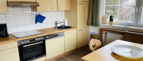 A compact kitchen with wooden cabinets, a built-in oven, a sink, and a window with a view of greenery.