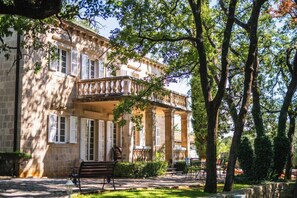A historic building with a balcony, stone columns, and a bench in the foreground.