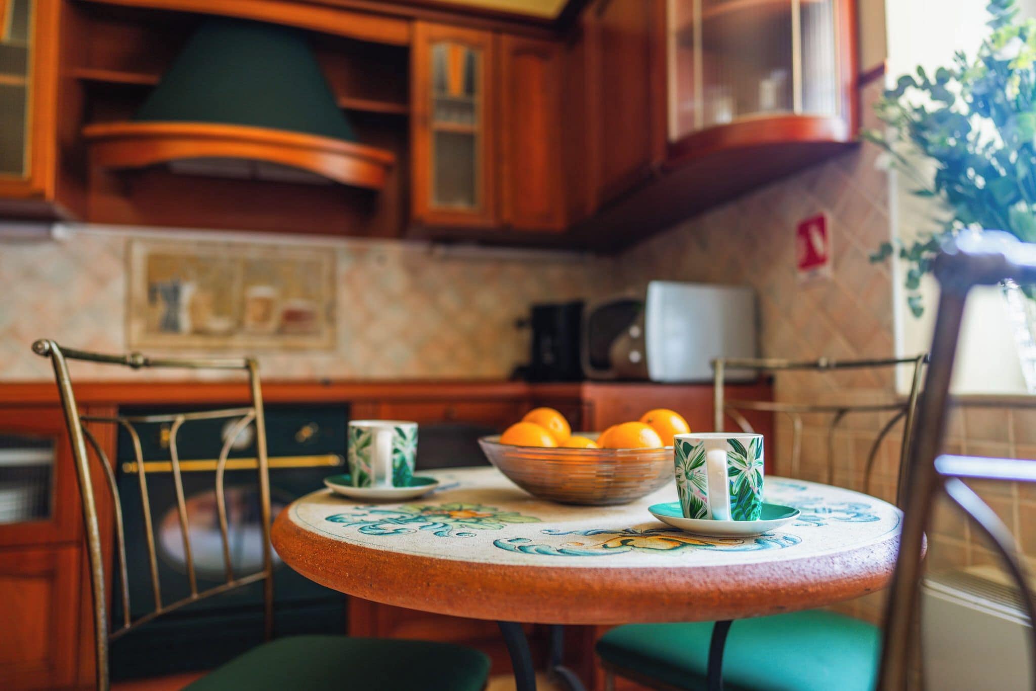 Una cocina con armarios de madera, microondas y una mesa con un bol de naranjas y tazas a juego.