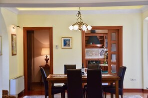 A dining area with a wooden table, black chairs, a chandelier, and a kitchen visible through a glass door.
