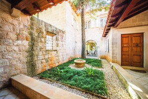 A courtyard with stone walls, a wooden door, and a small garden area with a fountain.