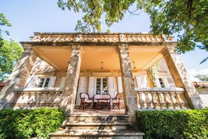 A stone building with a covered porch, columns, and a table with chairs. - Villa Tereza (Konavle)