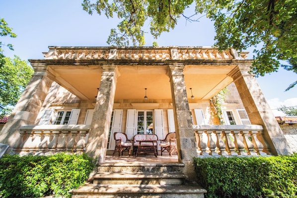 A stone building with a covered porch, columns, and a table with chairs. - Villa Tereza (Konavle)