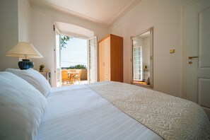 A hotel room with a large bed, a bedside lamp, an open door leading to a balcony, and a wooden wardrobe.
