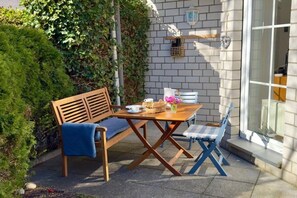 Ein Außenbereich mit Holztisch und -stühlen, einer Bank und einem kleinen Tisch mit Korb und Blumen.