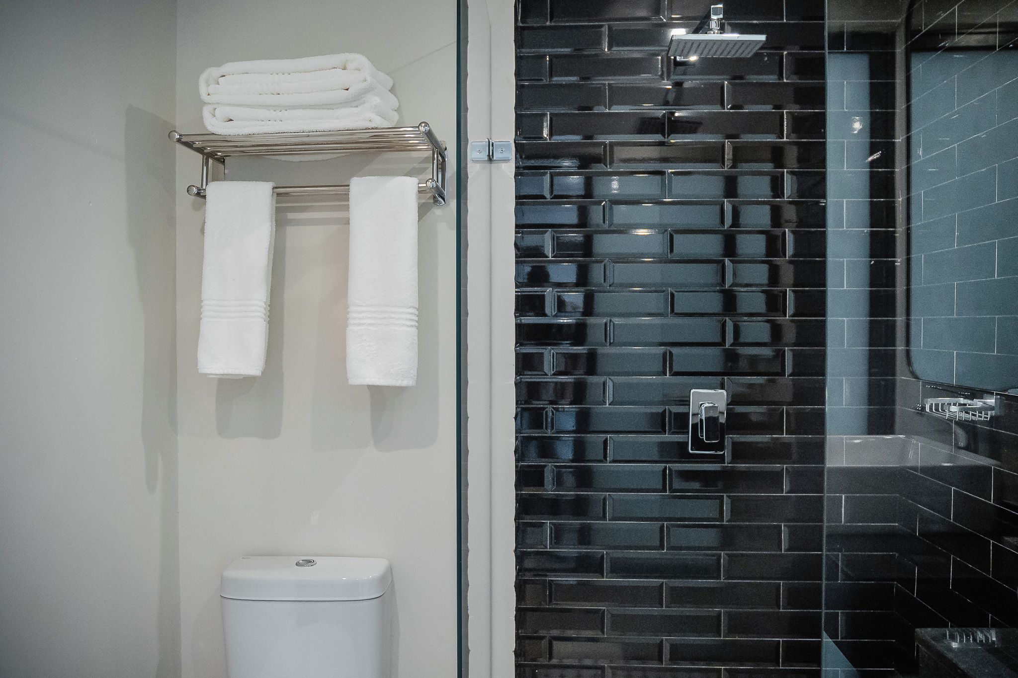 Ein Badezimmer mit schwarzem Duschwandfliesen, einer weißen Toilette und einem Handtuchhalter mit gefalteten Handtüchern.