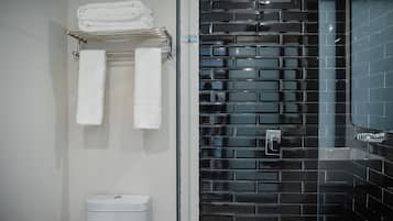 Ein Badezimmer mit schwarzem Duschwandfliesen, einer weißen Toilette und einem Handtuchhalter mit gefalteten Handtüchern.