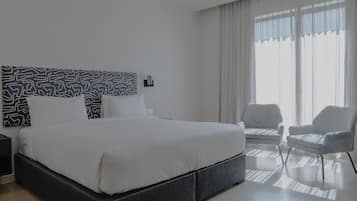 Ein modernes Hotelzimmer mit einem großen Bett, einem Nachttisch, einem Sessel und einem Fenster mit Vorhängen.