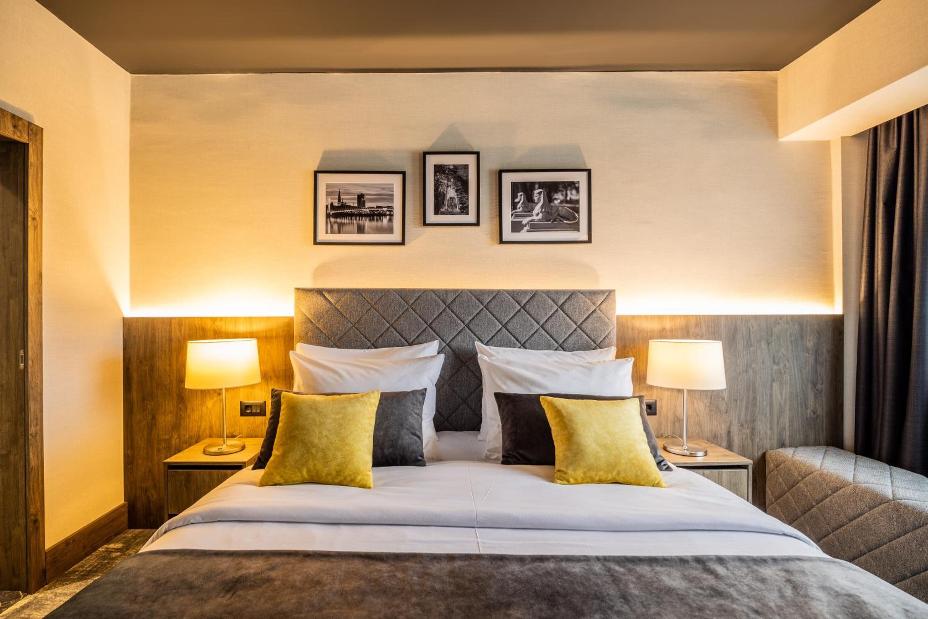 Habitación de hotel con una cama, dos lámparas de noche, un cabecero y tres cuadros en la pared.