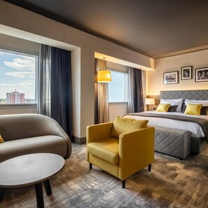 Habitación de hotel con cama, una silla, una mesa redonda y vista a la ciudad.