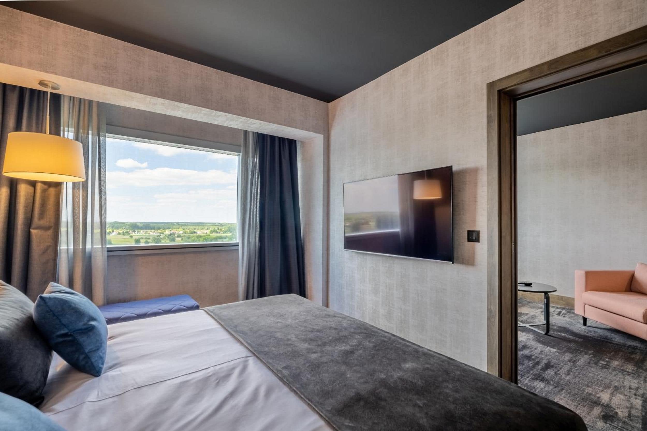 A hotel room with a bed, a TV, a sofa, and a view of the outdoors.
