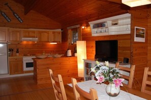 Een houten blokhut van binnen, met een keuken, eethoek en een televisie.