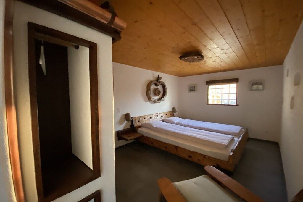 A room with a wooden ceiling, a bed with a headboard, a small window, and a wall-mounted light fixture.