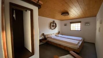 Ein Zimmer mit Holzboden, einem Bett mit Kopfteil, einem kleinen Fenster und einer Wandleuchte.