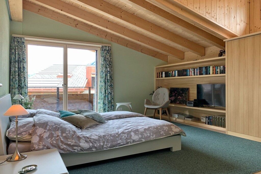 Ein Schlafzimmer mit einem Bett, einem Schreibtisch, einem Sessel, einem Bücherregal und einem Fernseher.