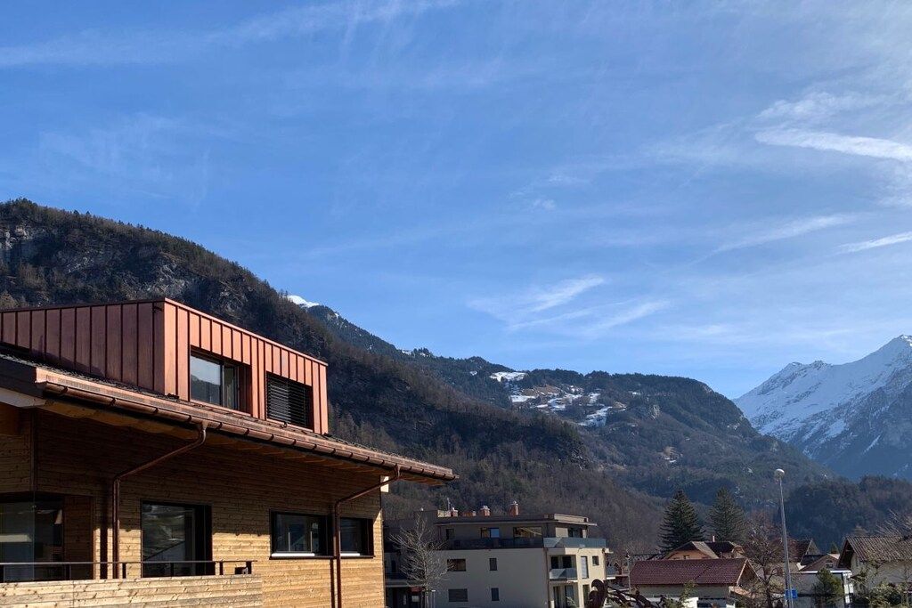 A mountain cabin with a wooden exterior, a balcony, and a view of snow-capped mountains.
