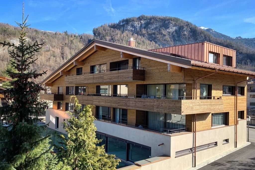 A multi-story building with balconies, large windows, and a mountainous backdrop.