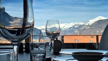 Ein Esstisch mit einem Weinglas, einem Wasserglas und einer Schüssel, gedeckt für eine Mahlzeit. Der Tisch steht im Freien mit Blick auf die Berge.