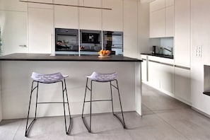 Une cuisine moderne dotée d’un îlot central, de deux tabourets de bar et donnant sur l’espace repas.