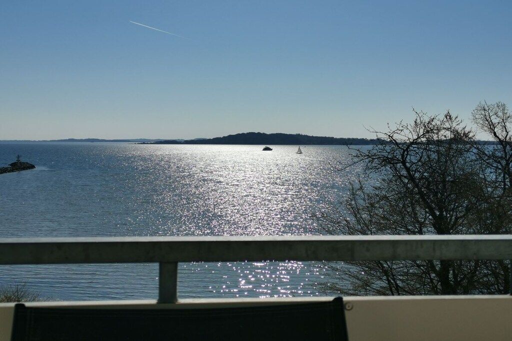 A body of water with a boat and a sailboat, a distant landmass, and a tree in the foreground.