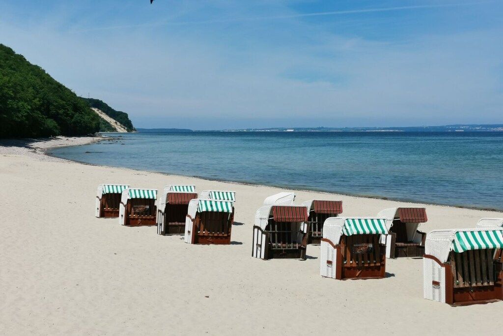 A beach with rows of beach chairs and umbrellas, a sandy shore, and a calm sea.