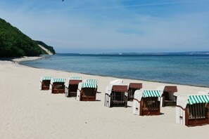 Ein Strand mit Liegestühlen und Sonnenschirmen, ein sandiger Uferstreifen und ein ruhiges Meer.