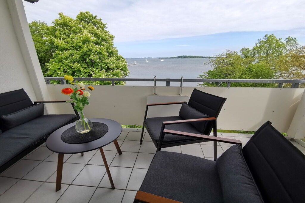 A balcony with a sofa, a small round table, and a vase of flowers.