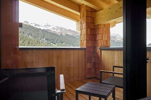 A wooden cabin with a view of mountains, a fireplace, and a table and chair set. - 5803 Alm-Lodge trais (Gargellen)