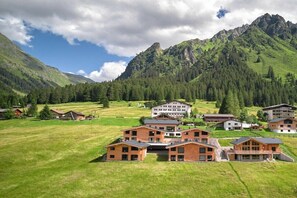 Een groep moderne gebouwen met een bergachtige achtergrond, omgeven door groene velden en dichte bossen.