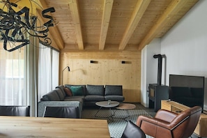 A modern living room with a wooden ceiling, a sectional sofa, a round coffee table, and a television. - 5803 Alm-Lodge trais (Gargellen)