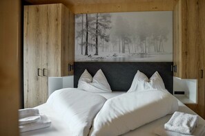 A bedroom with a large bed, white bedding, and a painting of a forest on the wall. - 5803 Alm-Lodge trais (Gargellen)