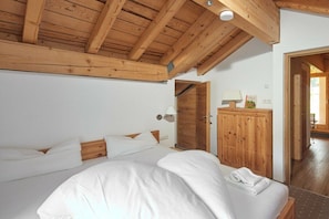 Ein Schlafzimmer mit Holzboden, einem Bett mit weißer Bettwäsche, einem Holzschrank und einer Tür zu einem anderen Raum.