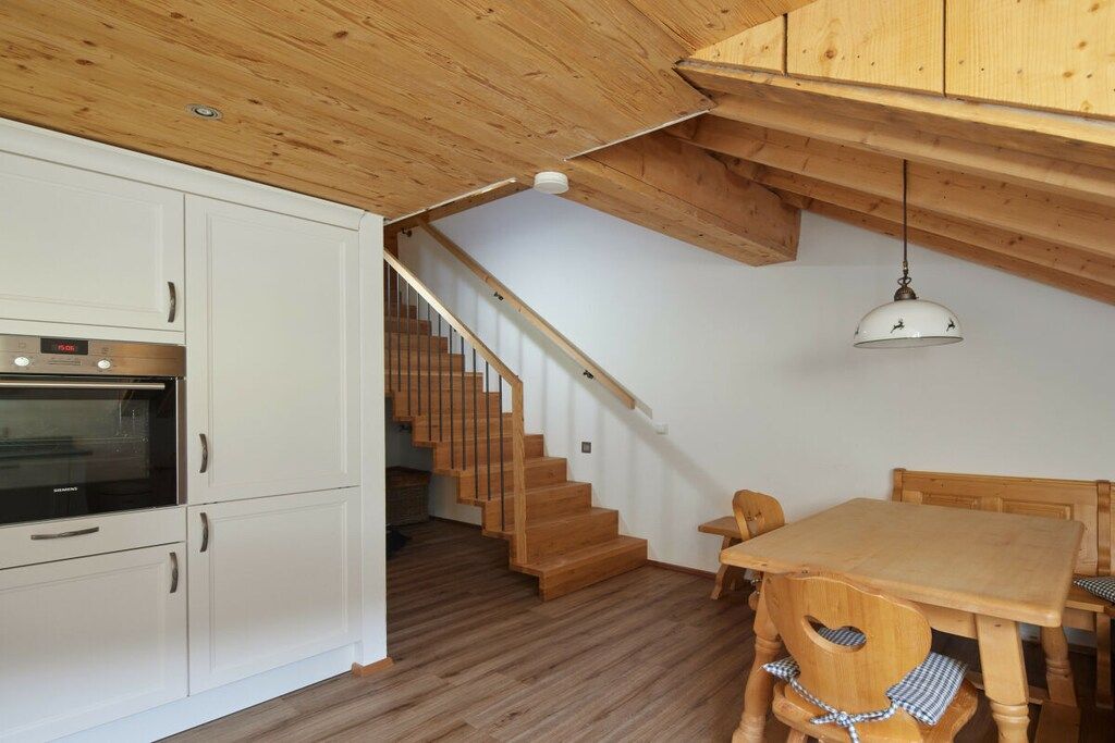 Una cocina con armarios blancos, una escalera de madera y un comedor con una mesa y sillas de madera.