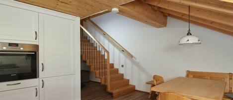 A kitchen with white cabinets, a wooden staircase, and a dining area with a wooden table and chairs.