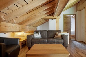 Een loft-achtige kamer met een schuine kap, een leren bank, een houten salontafel en een lamp.