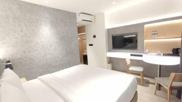 A modern hotel room with a large bed, a desk with a chair, a television, and a minibar.
