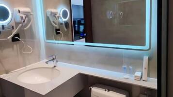 A modern bathroom with a large mirror, a sink, and a toilet.