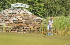 A person playing golf at Adventure Golf, with a stone wall and greenery in the background.