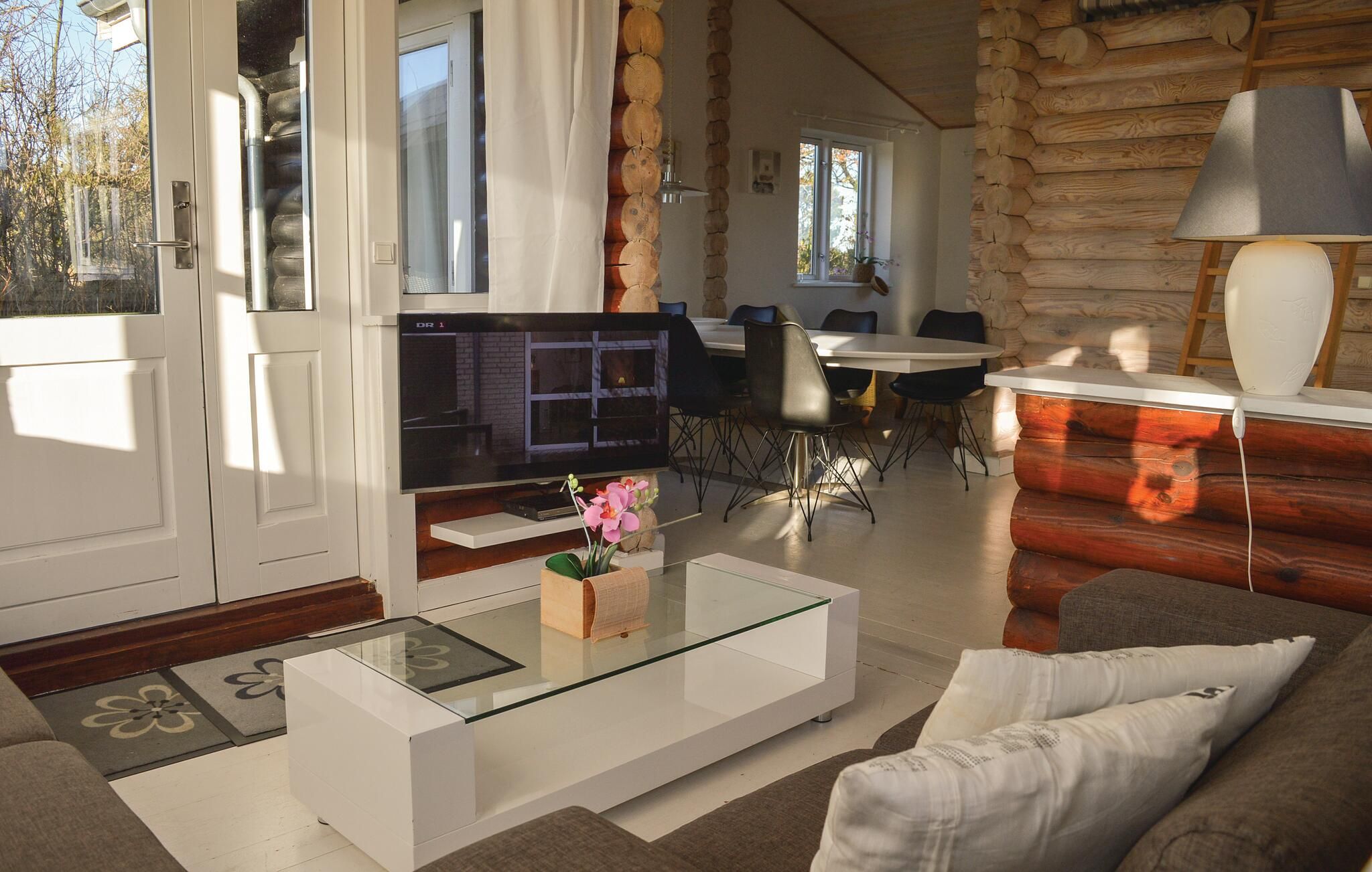 En moderne stue med sovesofa, glasbord, fjernsyn og spiseplads med stole og bord.
